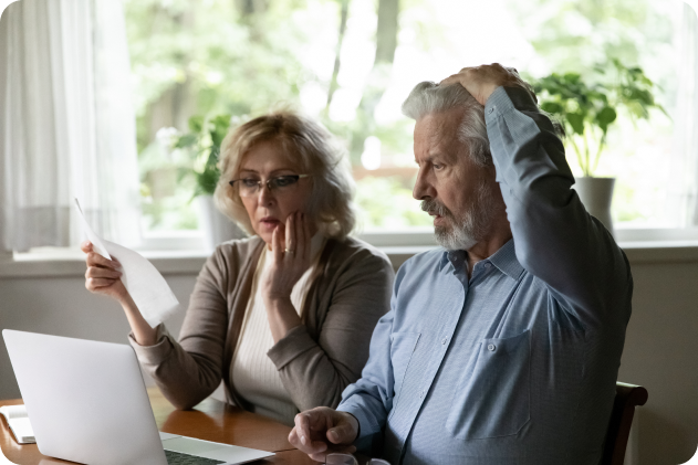 Senior couple looking concerned while reviewing documents and using a laptop